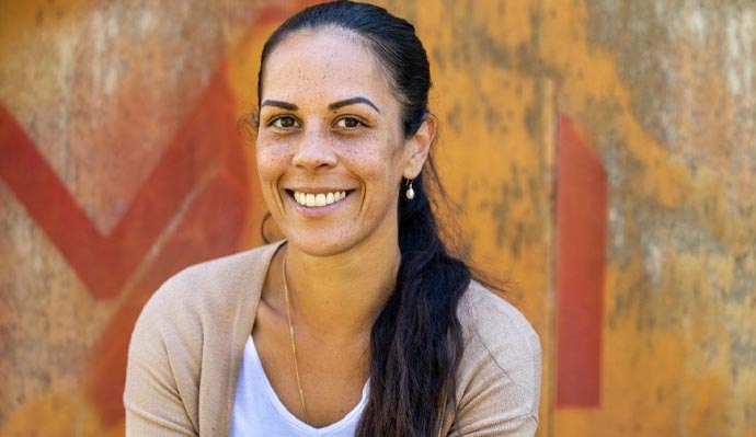A woman with brown eyes, dark hair and freckles smiling at the camera