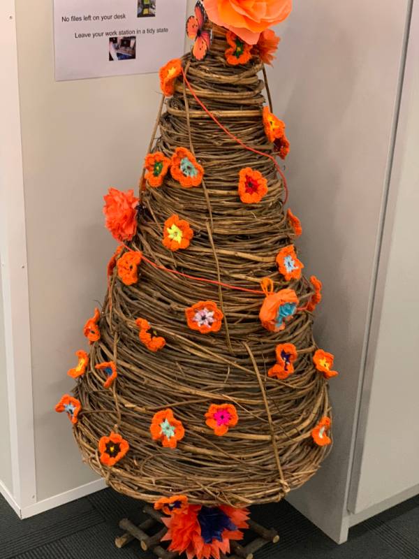 A wicker tree with orange crochet flowers for 16 Days of Activism