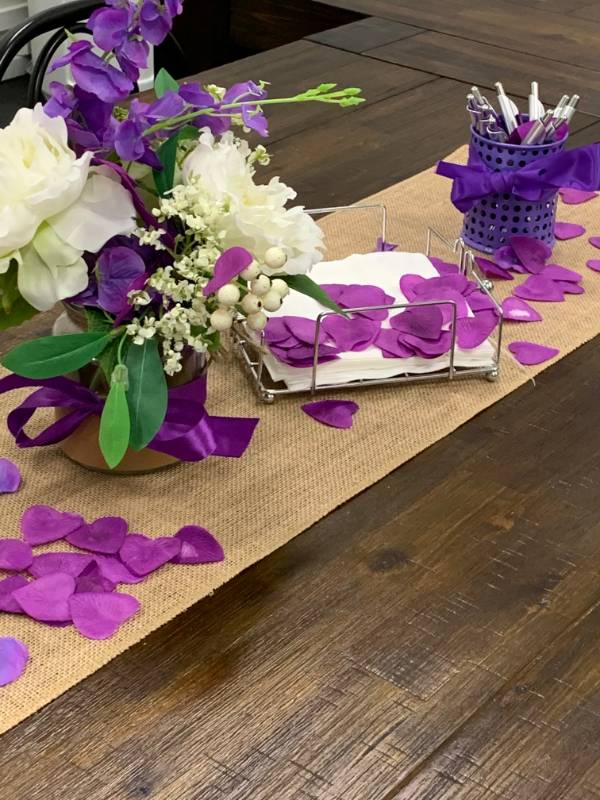 Purple and white flowers, napkins, and pens in a purple cup with a bow