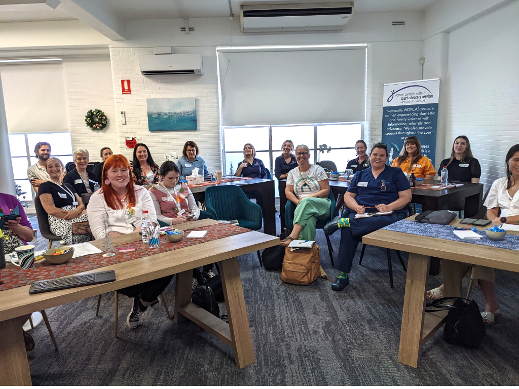 A group of disability and domestic violence service providers at the Women's Safety Hub. They are seated in a collaborative workshop and smiling.